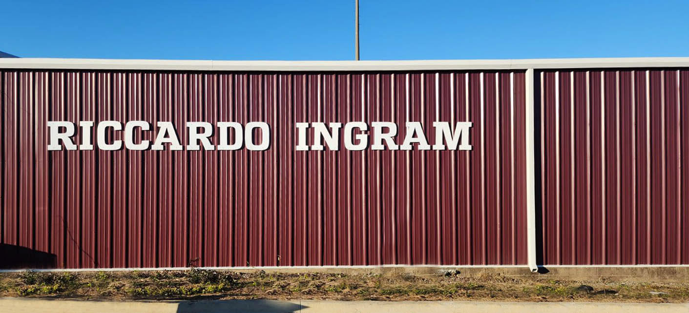 Routed plastic signage displaying the words "Riccardo Ingram" mounted on the side of Coffee High School's Riccardo Ingram hitting facility.