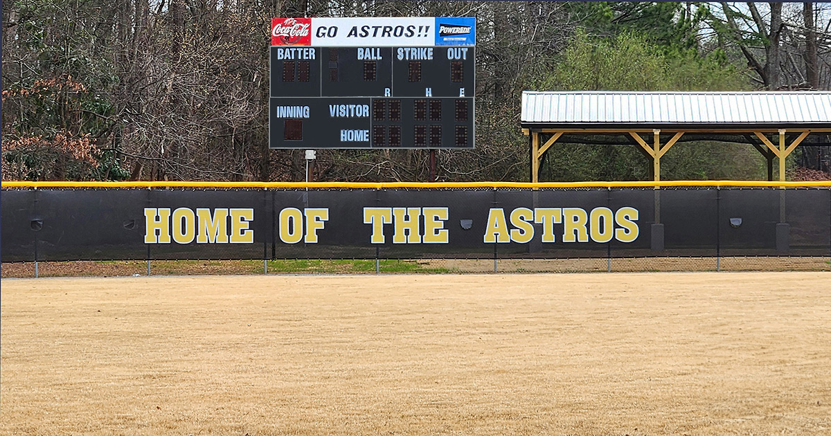 black fence windscreen printed with yellow lettering with a white outline reading 'home of the astros', affixed to a fence around a baseball field, topped with a yellow fence guard rail top tear drop fence cap