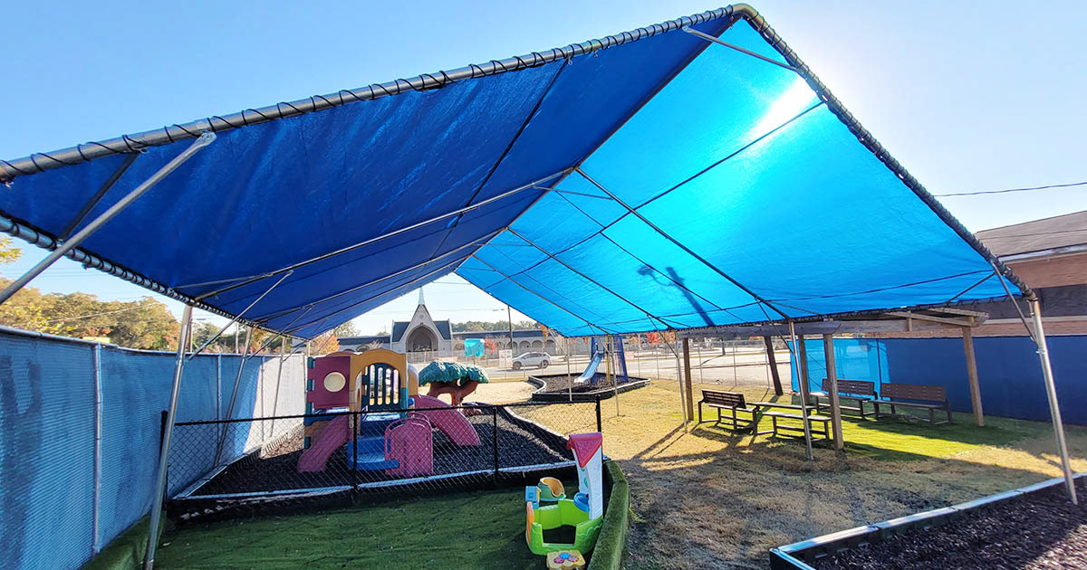 A play area beneath a large, metal-framed blue shade structure shaped like a pavilion. 