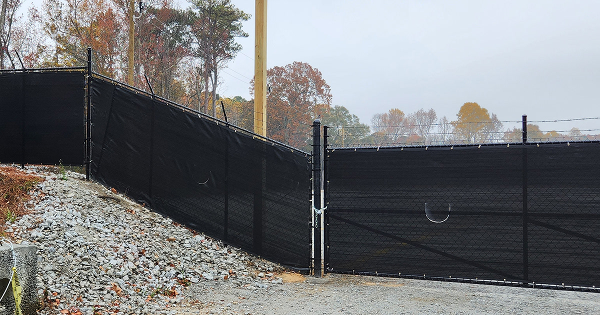 Close-up of a fence surrounding a business, covered with black privacy windscreen, highlighting challenging installation angles.