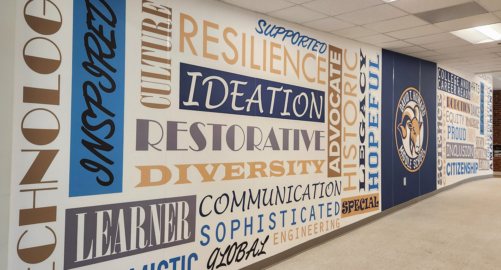 A floor-to-ceiling adhesive vinyl wall mural featuring a blue square with a seal in the middle, and word grids to the left and right of the square. The word grid on the left includes the words 'HOPEFUL', 'SPECIAL', 'LEGACY', 'HISTORY', 'IDEATION', 'ADVOCATE', 'COMMUNICATION', 'DIVERSITY', 'RESILIENCE', 'SOPHISTICATED', 'SUPPORTED', 'RESTORATIVE', 'LEARNER', 'OPTIMISTIC', 'GLOBAL', 'ENGINEERING', 'INSPIRED', and 'TECHNOLOGY' in various colors and fonts over a white background. In the middle, the seal consists of a ram head image inside a circle with a white background, surrounded by a blue ring with the words 'DAVID T. HOWARD MIDDLE SCHOOL' in white, and a goldenrod ring around the blue ring. The word grid on the right contains the words 'CAREER', 'SCIENCE', 'CREATIVITY', 'ROBOTICS', 'EQUITY', 'PROUD', 'INCLUSIVE', and 'CITIZEN' in various colors and fonts over a white background. 