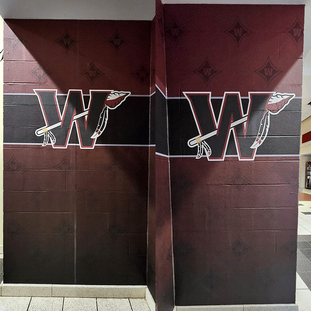 Two identical adhesive vinyl wall murals on different walls. Both murals feature a full-print burgundy gradient background with a black banner at the top, outlined in white, in the center of this banner is a large black 'W' logo, outlined in burgundy and white, with an arrow weaved through the letter.