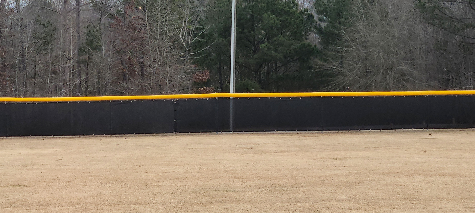 black fence windscreen with half moon vents, black zip ties and brass grommets surrounding a baseball field, fence topped with yellow poly-cap corrugated rail top fence cap