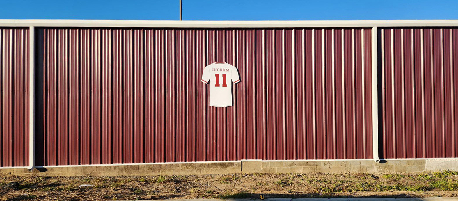A close-up of the back of a large routed plastic baseball shirt featuring the name "Ingram" and the number "11" on the back. The plastic signage is mounted on the side of Coffee High School's Riccardo Ingram hitting facility.