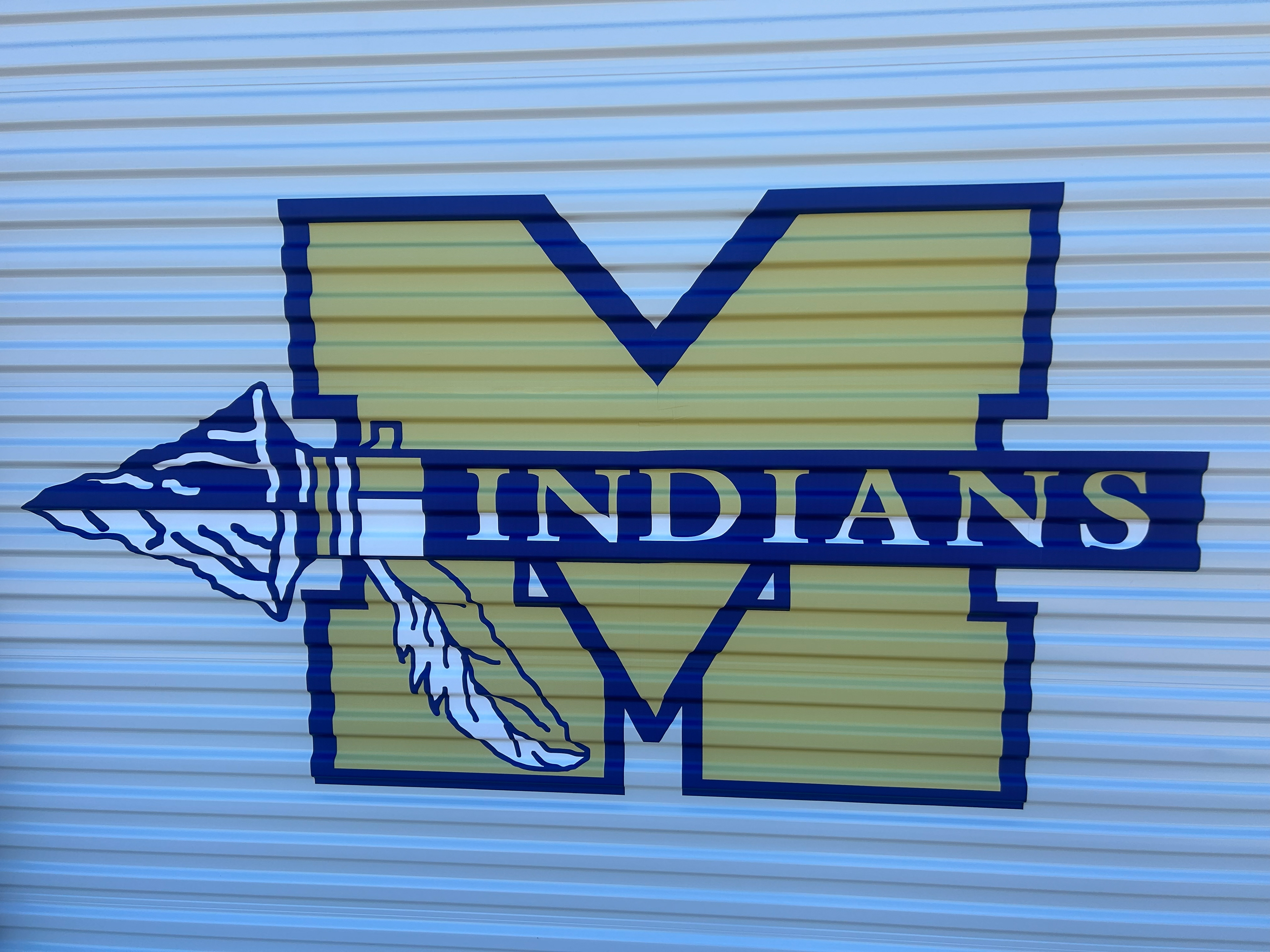Close-up front view of a large custom-designed vinyl sports team logo adhered to a metal rolling garage-style door on a barn-style school building.