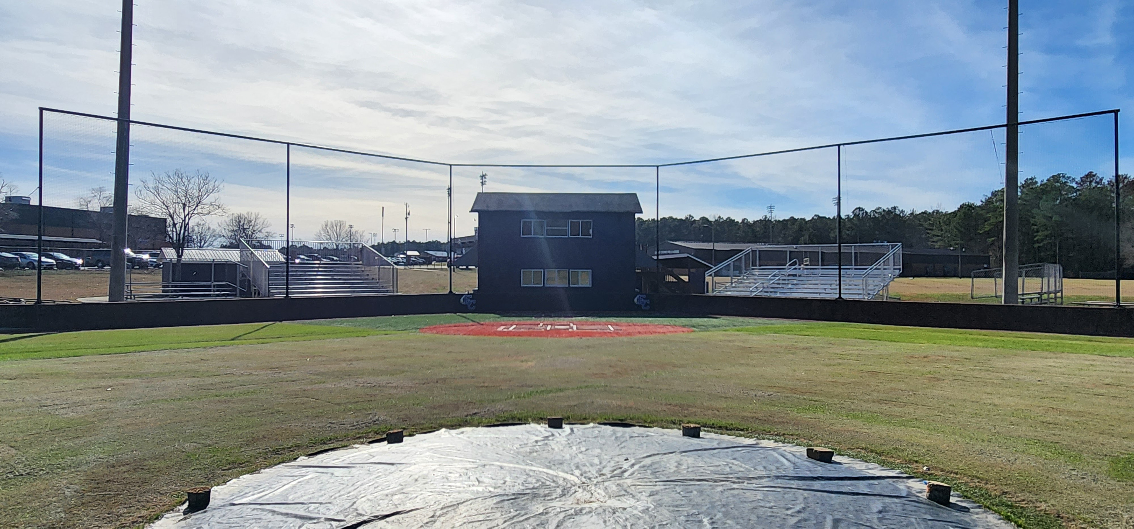 backstop black sports netting surrounding the catcher's box above black sports vinyl covered backstop padding printed with blue 'EC' logo with white outline and white and yellow feather accents, attached to a brick wall