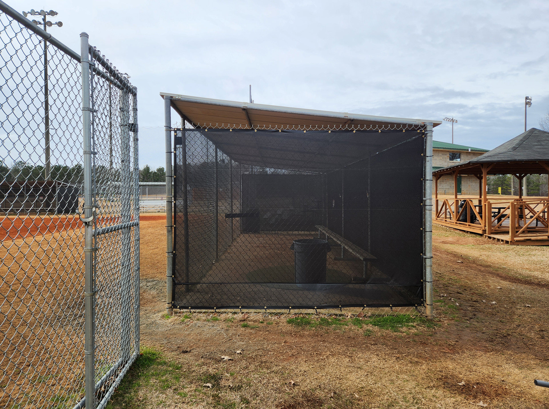 black fence windscreen with half moon vents, black zip ties and brass grommets surrounding a baseball field dugout