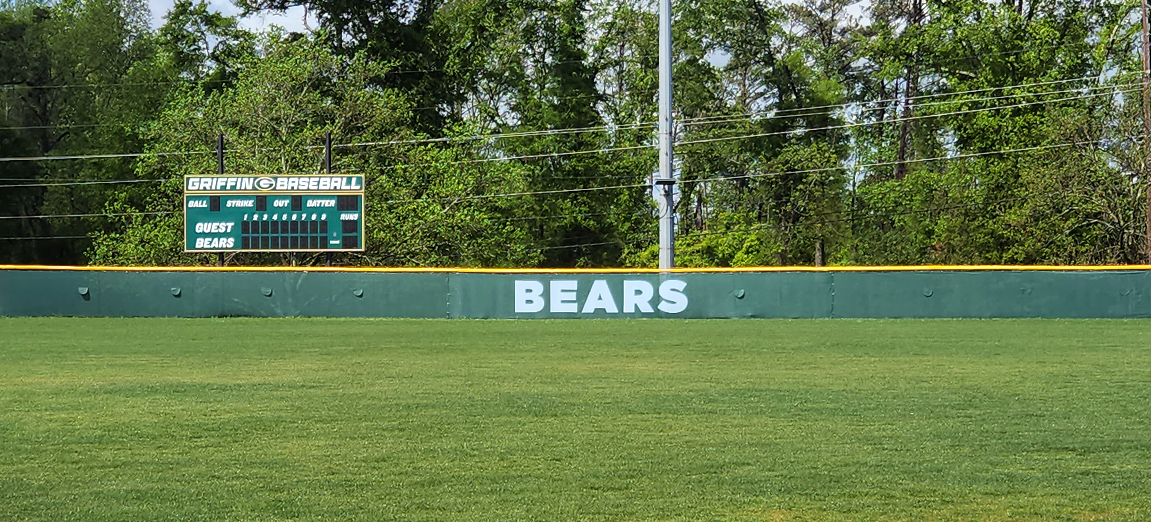 Long shot of dark forest green windscreens that are branded with a green, white and yellow 'G' logo and text reading 'BEARS' attached to a fence with a yellow corrugated poly cap rail top fence cap.