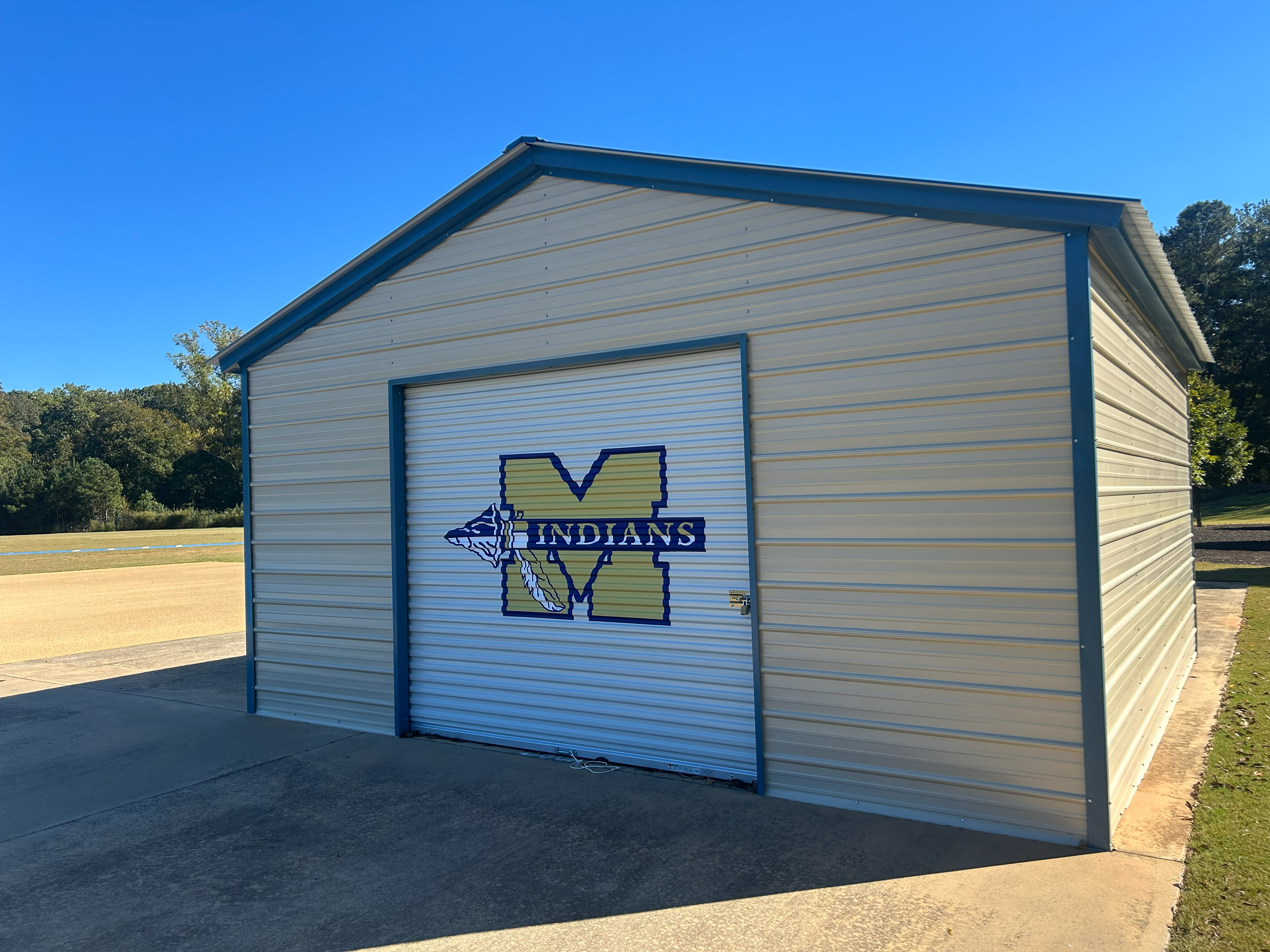 Large custom-designed vinyl sports team logo adhered to a metal rolling garage-style door on a barn-style school building, viewed from the side.