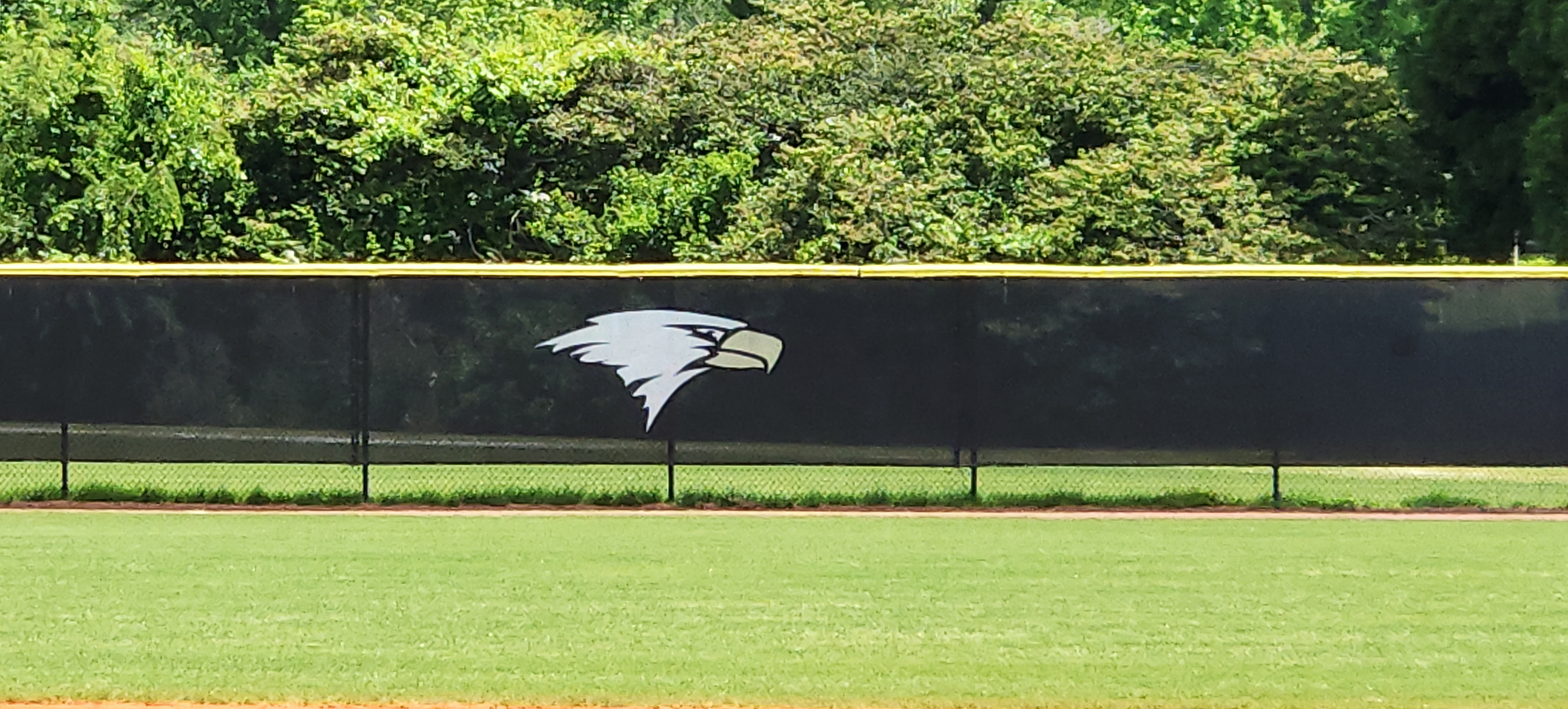 Closeup of black windscreen branded with an eagle logo affixed to a fence topped with yellow fence cap.
