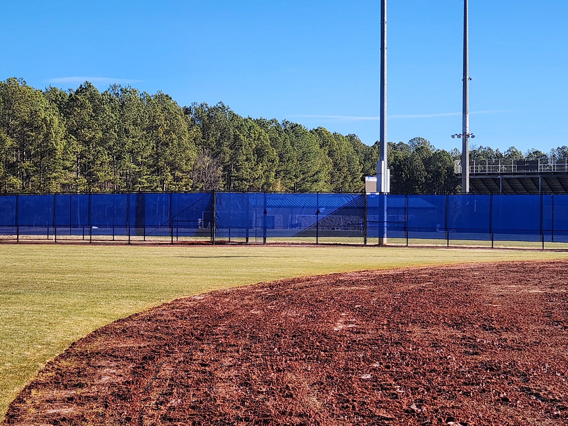blue windscreen attached to a fence barrier on the outter edge of a baseball field
