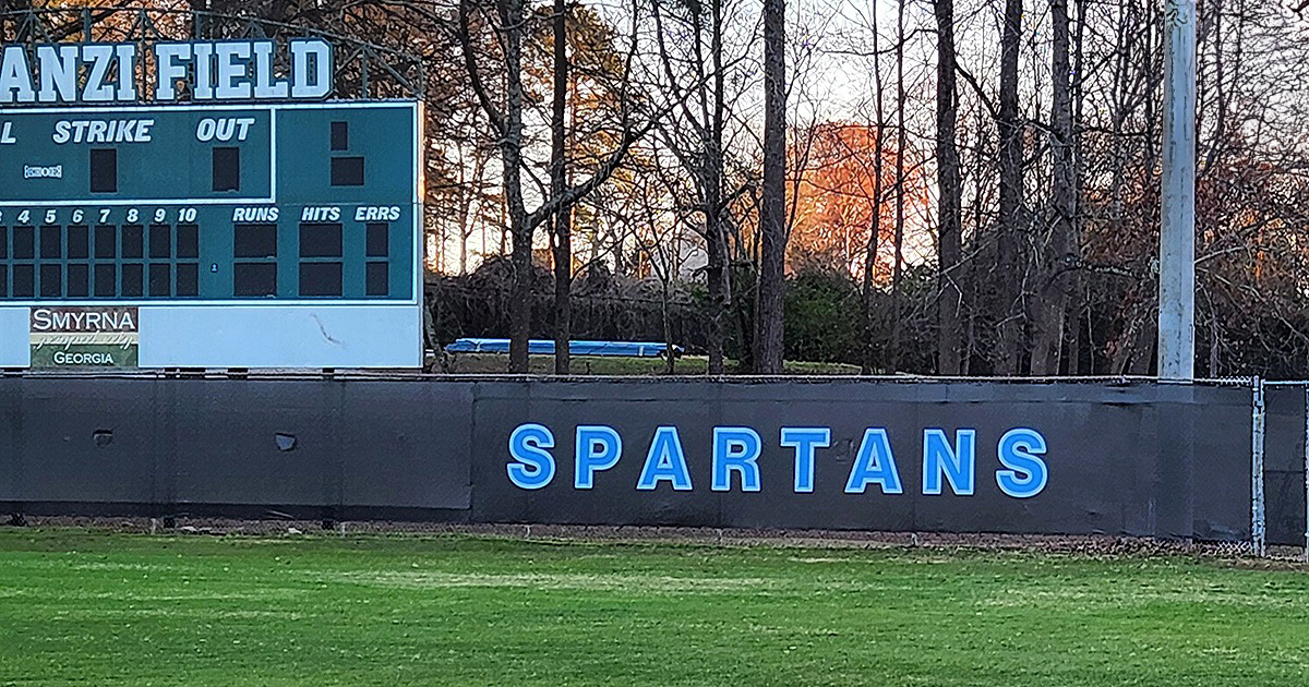 black fence windscreen printed with blue lettering outlined in a lighter shade of blue reading 'Spartans' in a baseball outfield
