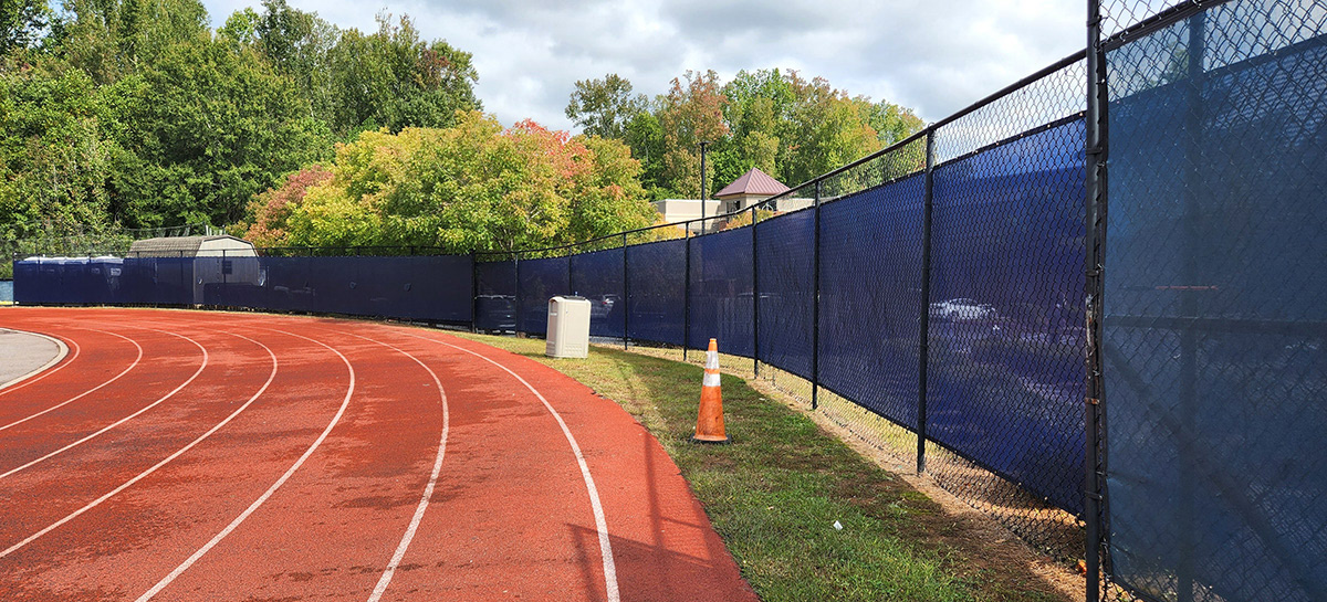 Navy blue fence windscreen separates the running track surrounding the football field from the pedestrian area outside.