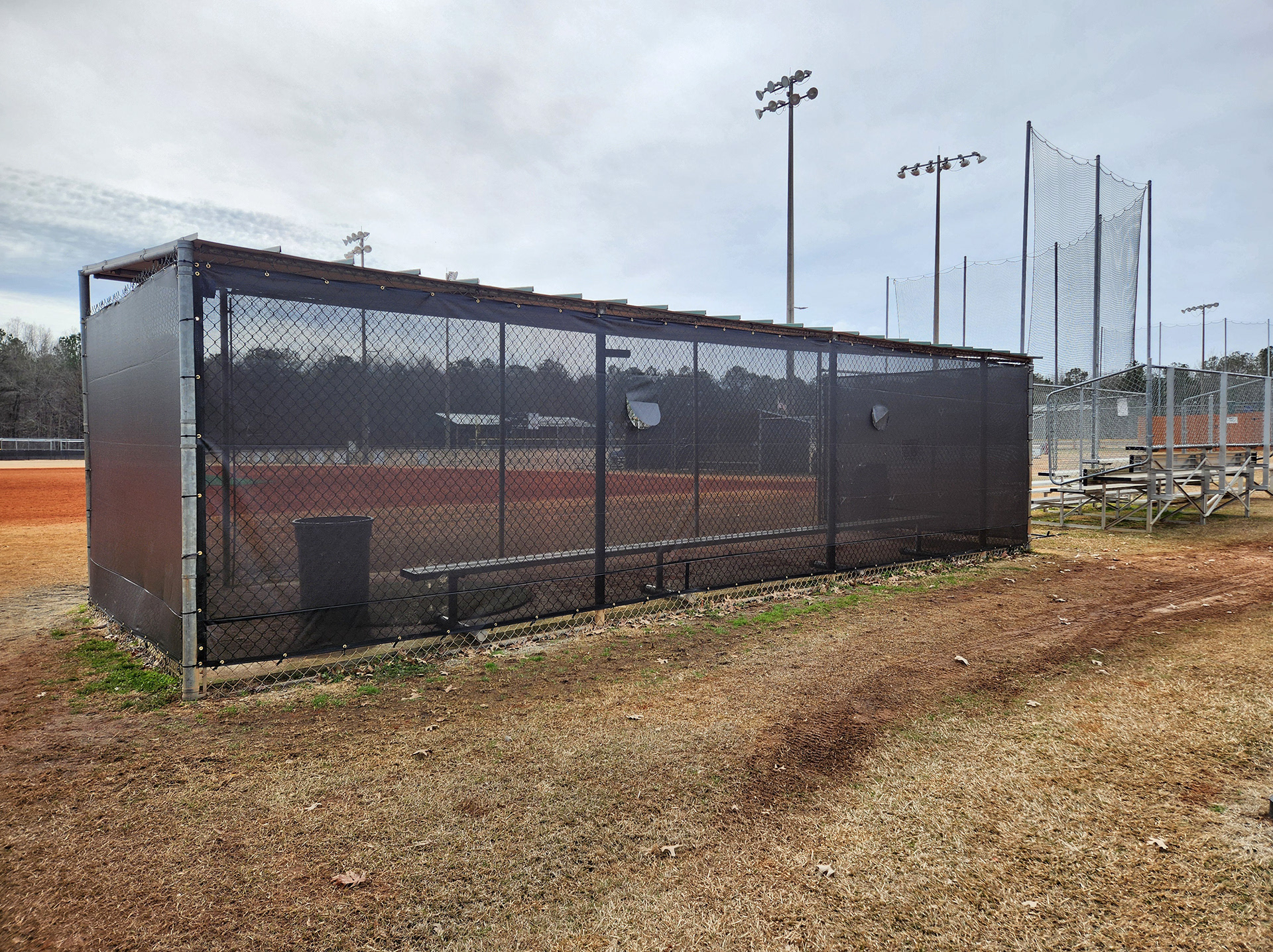 black fence windscreen with half moon vents, black zip ties and brass grommets surrounding a baseball field dugout