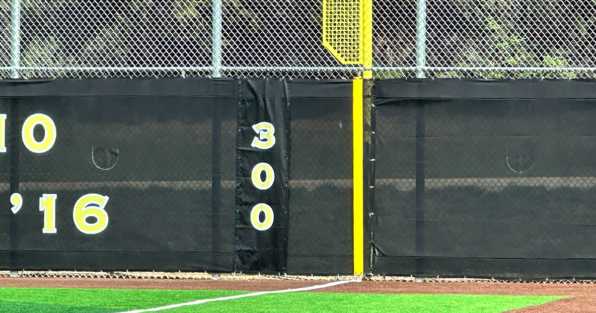 Closeup of black windscreen attached to a fence printed with yellow numbers with a white outline.
