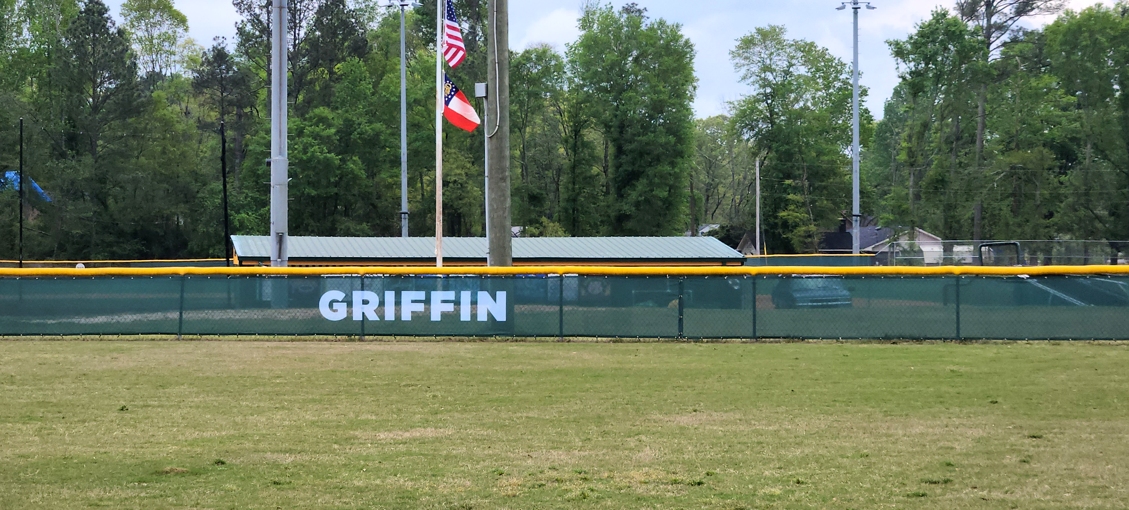 Near shot of dark forest green windscreens are branded with white text reading 'Griffen' attached to a fence with a yellow corrugated poly cap rail top fence cap.