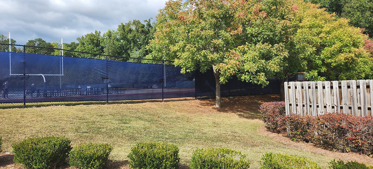 A Navy blue fence windscreen is positioned behind the goal, separating the football field from an outside grassy area.