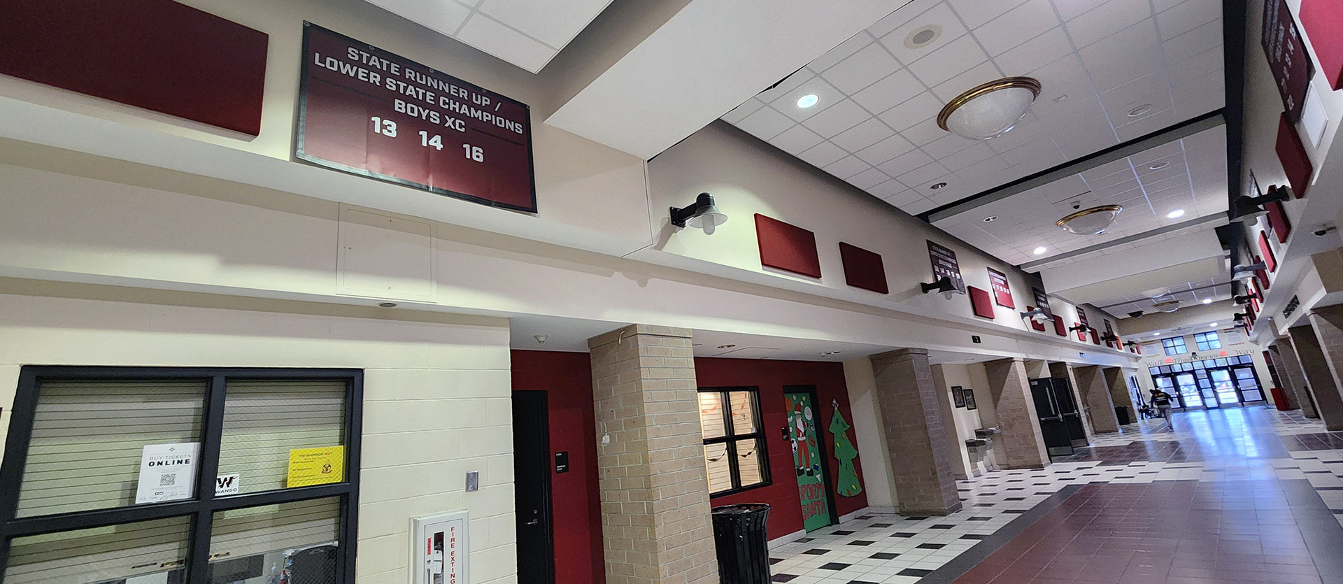 A maroon 10oz VCP windscren rectangular banner with white text and numbers promoting state champions for Wando High School. The banner is displayed on the upper part of the hall walls, lining the hall.