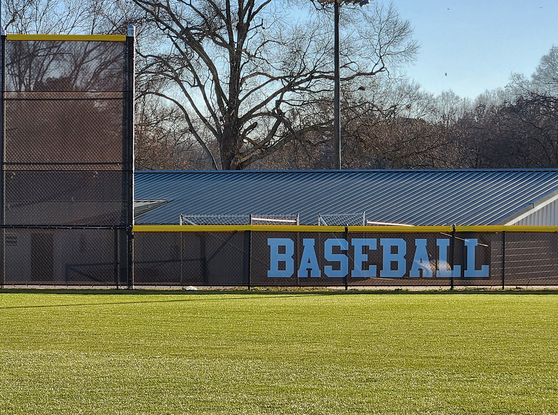 fence surrounding baseball field with black fence windscreen printed with white text reading 'baseball' and yellow D-style safety top cap
