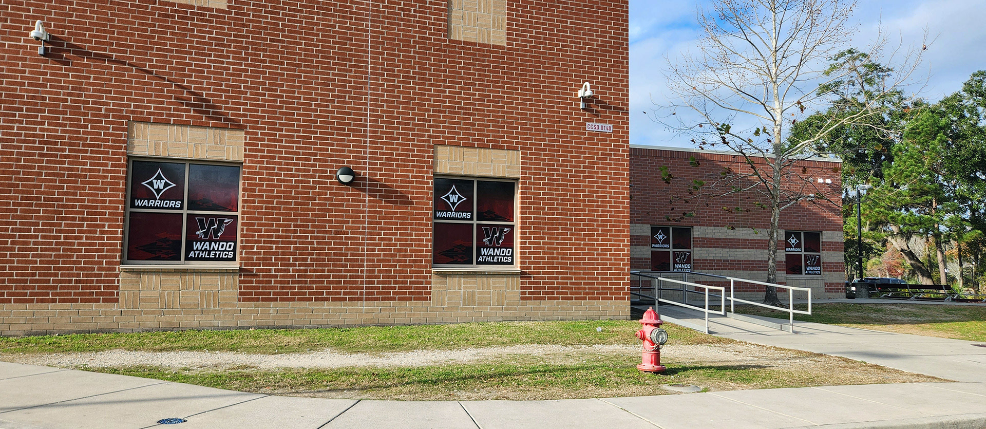 Four identical window perforations on different windows, each with a dark red translucent background. In the top left corner of each window, there is a navy four-point star logo, outlined in white and red, with a 'W' in the center and the word 'Warriors' printed in white beneath the star. In the bottom right corner, a large black 'W' logo, outlined in burgundy and white, with an arrow weaved through the letter.