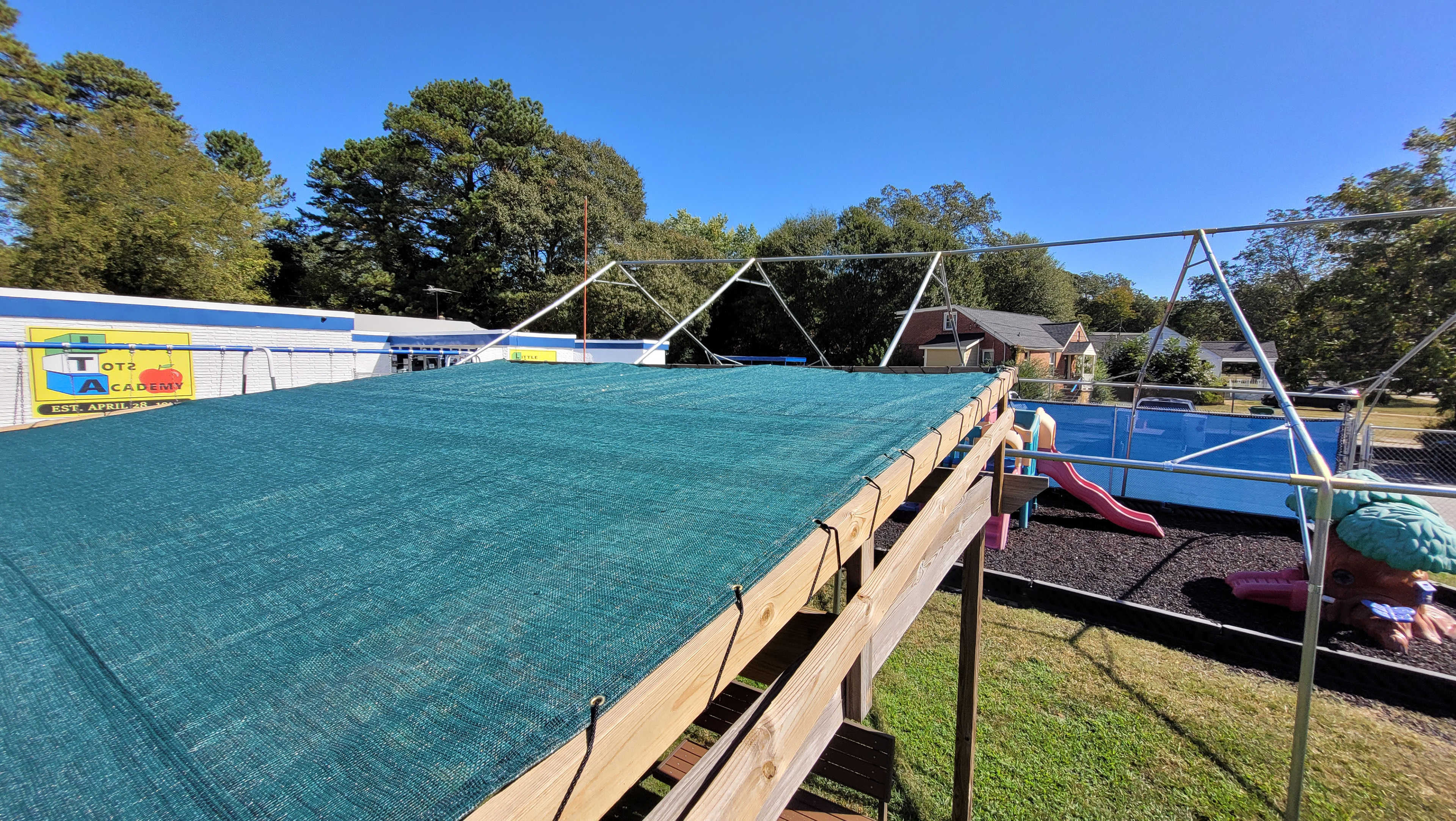 A seating area covered with a wood-framed, flat-roofed green shade structure, next to a metal-frame structure positioned above a play area.