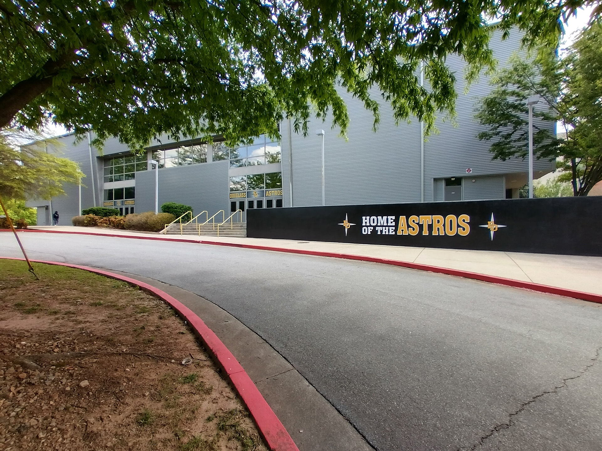 black fence windscreen printed with twp white four point star logos with 'FD' in yellow over them, and the text 'home of the Astros' printed between, in front of a grey building with window perf reading 'Douglass FD Astros' in yellow with a grey background