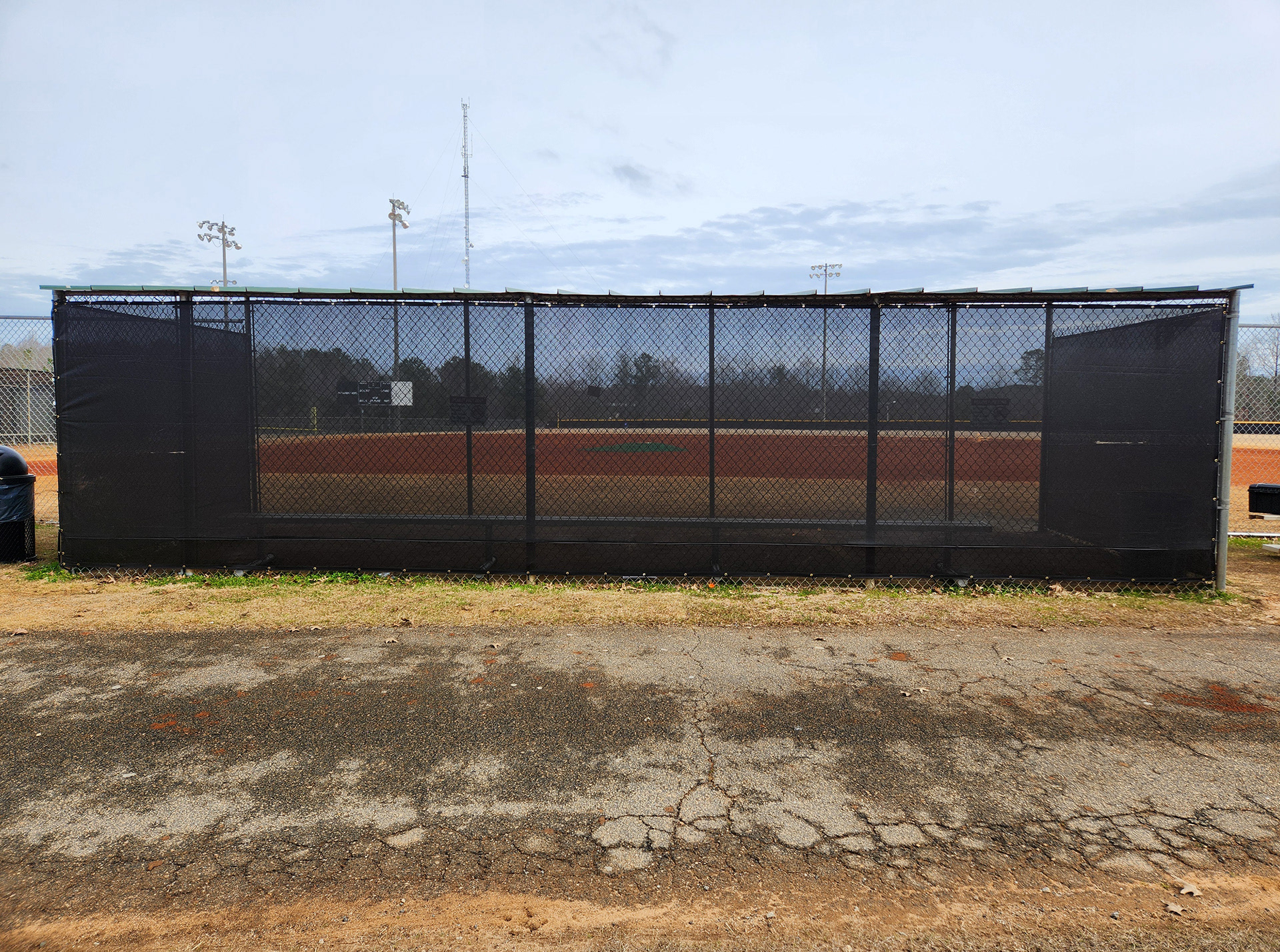 black fence windscreen with half moon vents, black zip ties and brass grommets surrounding a baseball field dugout
