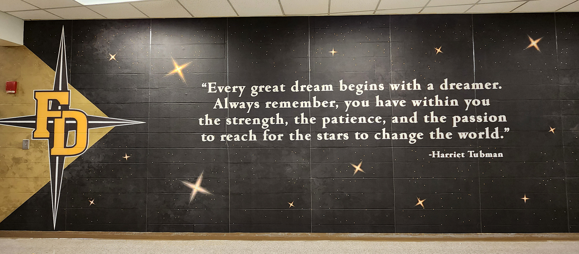 full print adhesive vinyl wall mural and window perf printed with gradient white and yellow stars on an all black background beneth the words "Every great dream begins with a dreamer. Always remember, you have within you the strength, the patience, and the passion to reach for the stars to change the world. - Harriet Tubman'' in white and a four point star logo to the left with 'FD' in yellow over it.