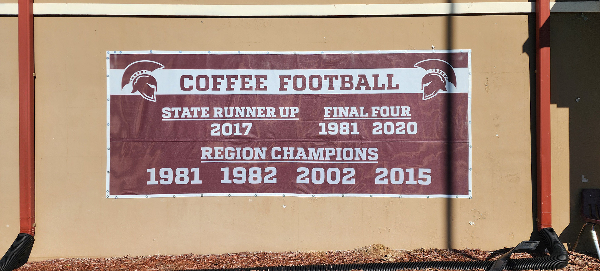 A windscreen banner displaying the years for state runner-up, Final Four, and region champion for 'Coffee Football', on Coffee Highschool's Ronnie Johnson Field House.
