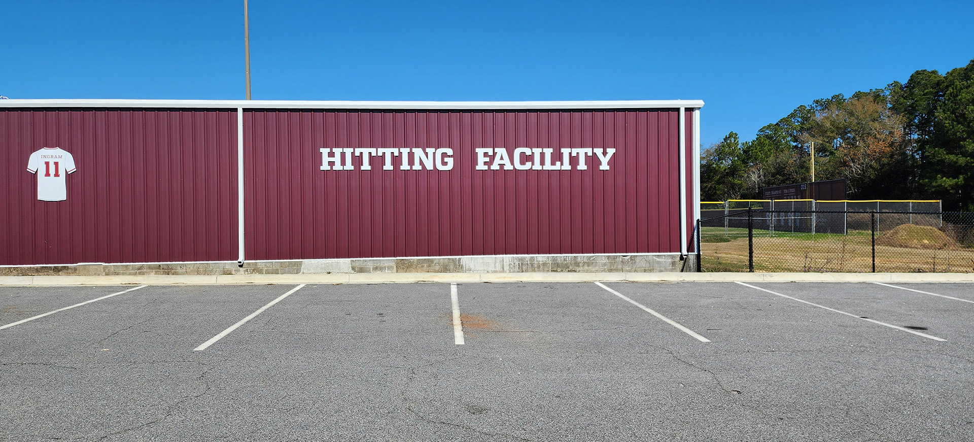 Routed plastic signage displaying the words "Hitting Facility" with a large routed plastic baseball shirt positioned to the left, mounted on the side of Coffee High School's Riccardo Ingram hitting facility.