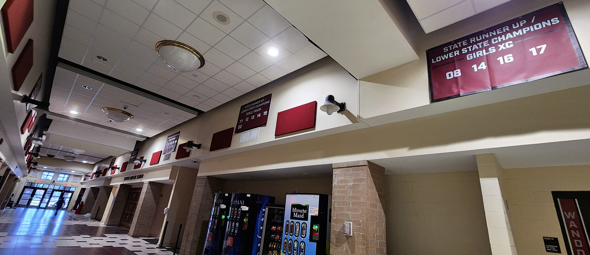 A maroon 10oz VCP windscren rectangular banner with white text and numbers promoting state champions for Wando High School. The banner is displayed on the upper part of the hall walls, lining the hall.
