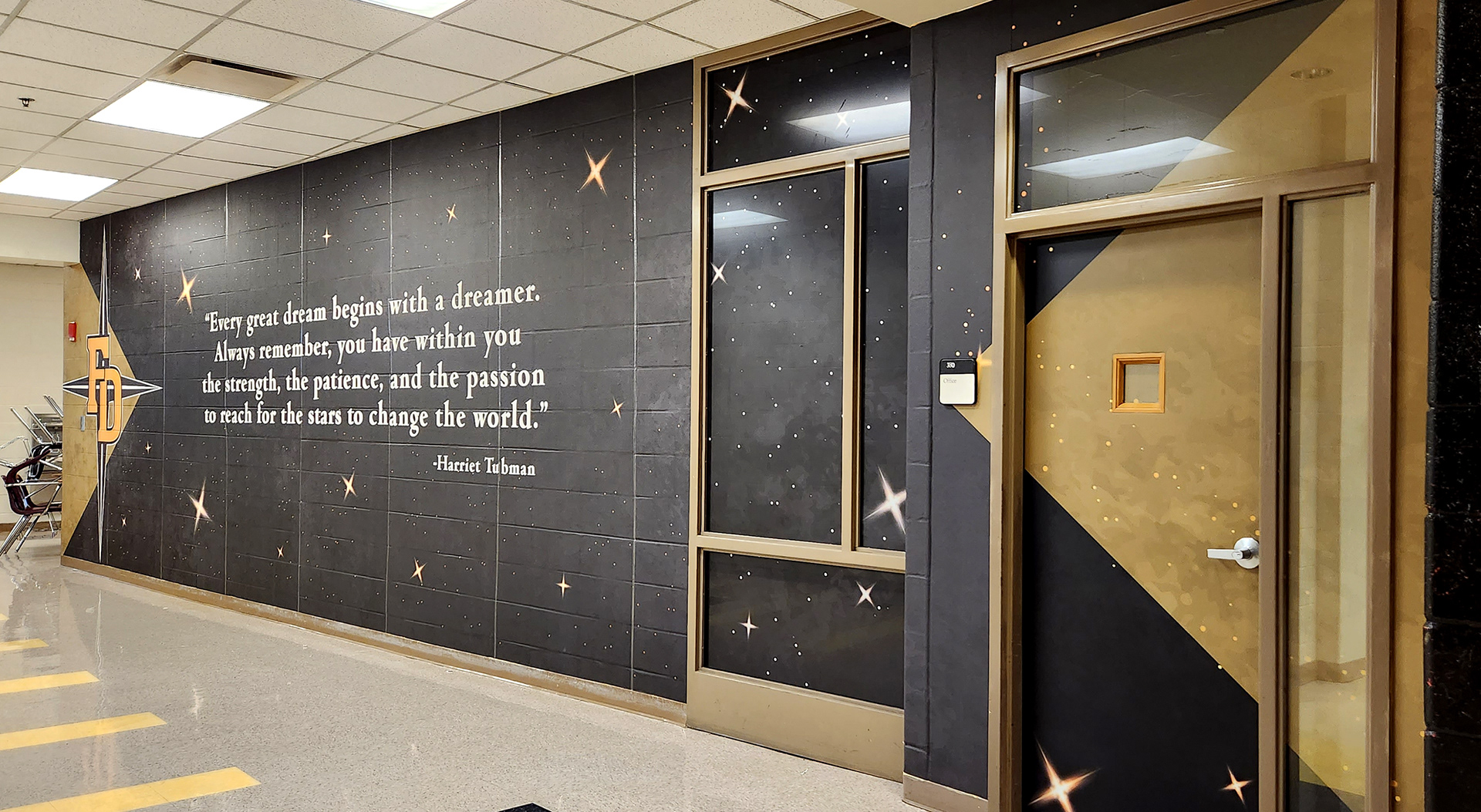 full print adhesive vinyl wall mural and window perf printed with gradient white and yellow stars on an all black background beneth the words "Every great dream begins with a dreamer. Always remember, you have within you the strength, the patience, and the passion to reach for the stars to change the world. - Harriet Tubman'' in white and a four point star logo to the left with 'FD' in yellow over it.