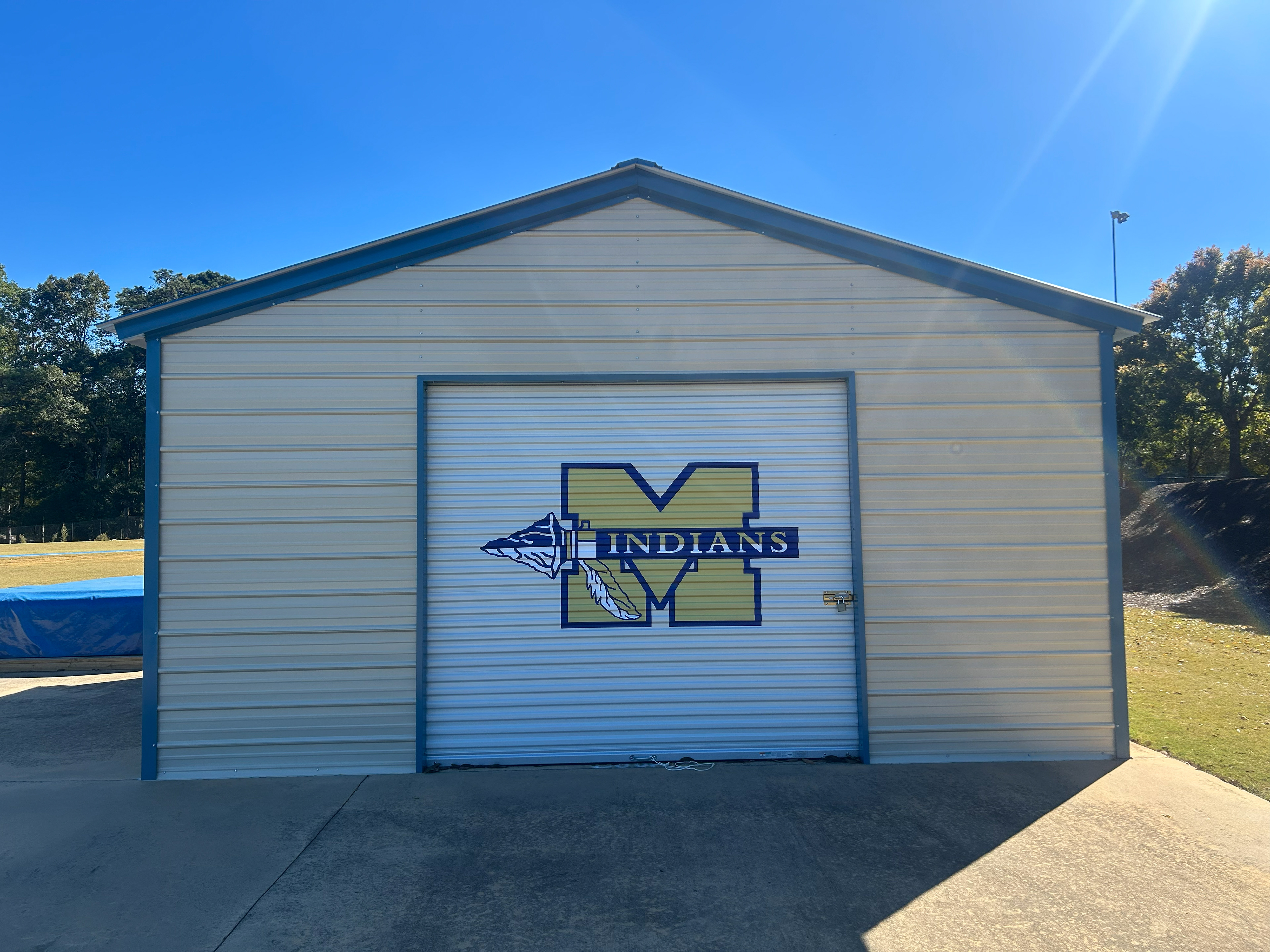 Large custom-designed vinyl sports team logo adhered to a metal rolling garage-style door on a barn-style school building, viewed from the front.