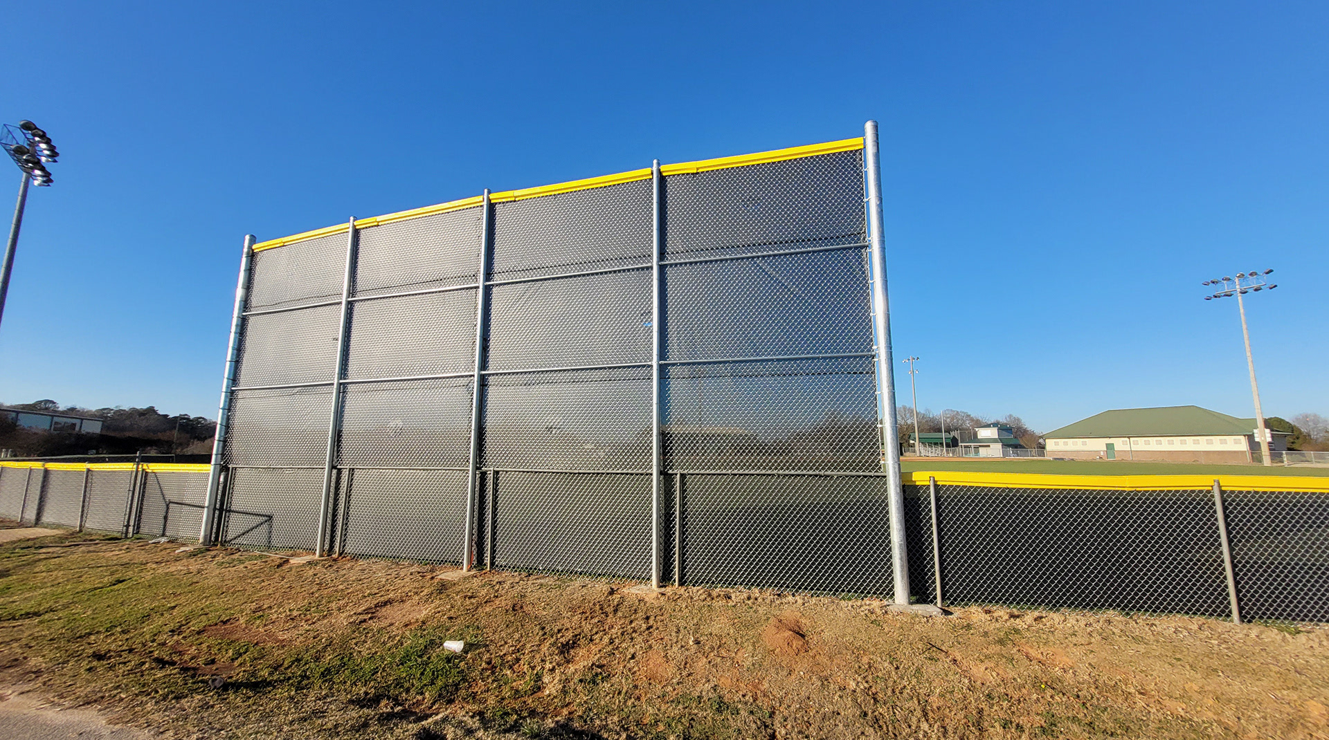 fence surrounding baseball field with the backside of black fence windscreen shown and yellow D-style safety top cap