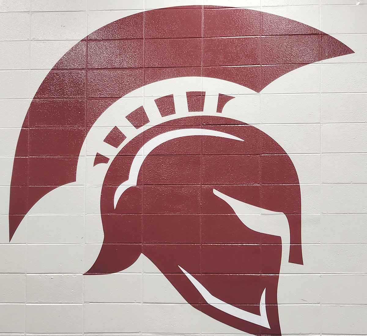 A painted white brick wall featuring adhesive vinyl decal of a Trojan helmet silhouette.