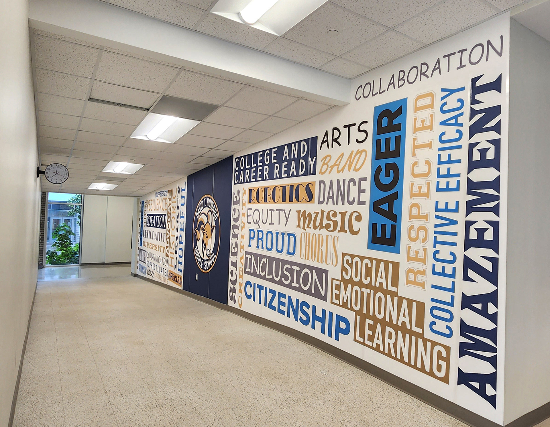 A floor-to-ceiling adhesive vinyl wall mural featuring a blue square with a seal in the middle, and word grids to both the right and left of the blue square. The word grid on the left contains the words 'HOPEFUL', 'SPECIAL', 'LEGACY', 'HISTORY', 'IDEATION', 'ADVOCATE', 'COMMUNICATION', 'DIVERSITY', 'RESILIENCE', 'SOPHISTICATED', 'SUPPORTED', 'RESTORATIVE', 'LEARNER', 'OPTIMISTIC', 'GLOBAL', 'ENGINEERING', 'INSPIRED', and 'TECHNOLOGY' in various colors and fonts on a white background. In the middle, the seal consists of a ram head image at the center of a circle with a white background, surrounded by a blue ring with the words 'DAVID T. HOWARD MIDDLE SCHOOL' in white, and a goldenrod ring around the blue ring. The word grid on the right contains the words 'CAREER', 'SCIENCE', 'CREATIVITY', 'ROBOTICS', 'EQUITY', 'PROUD', 'INCLUSIVE', and 'CITIZEN' in various colors and fonts on a white background. 