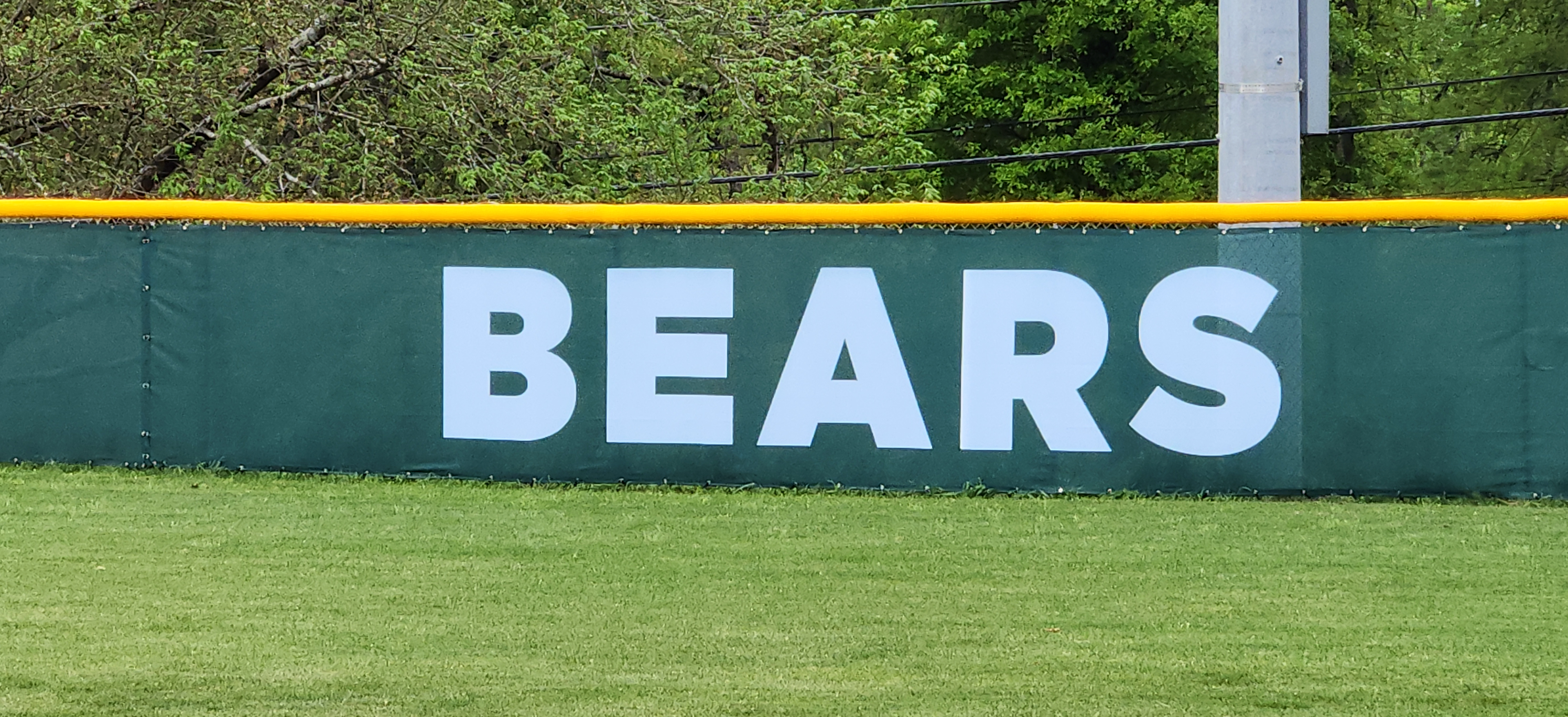 Closeup of dark forest green windscreens are branded with white text reading 'bears' attached to a fence with a yellow corrugated poly cap rail top fence cap.