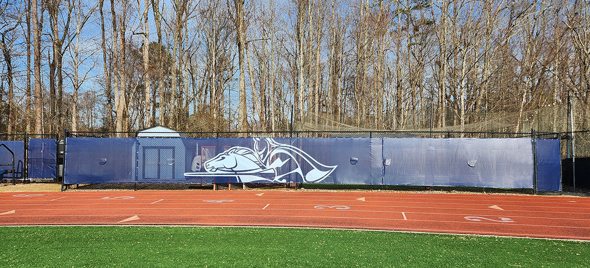 The front shot of navy blue fence windscreen panels alongside a football field features a white outline of a knight riding a horse in a jousting position.