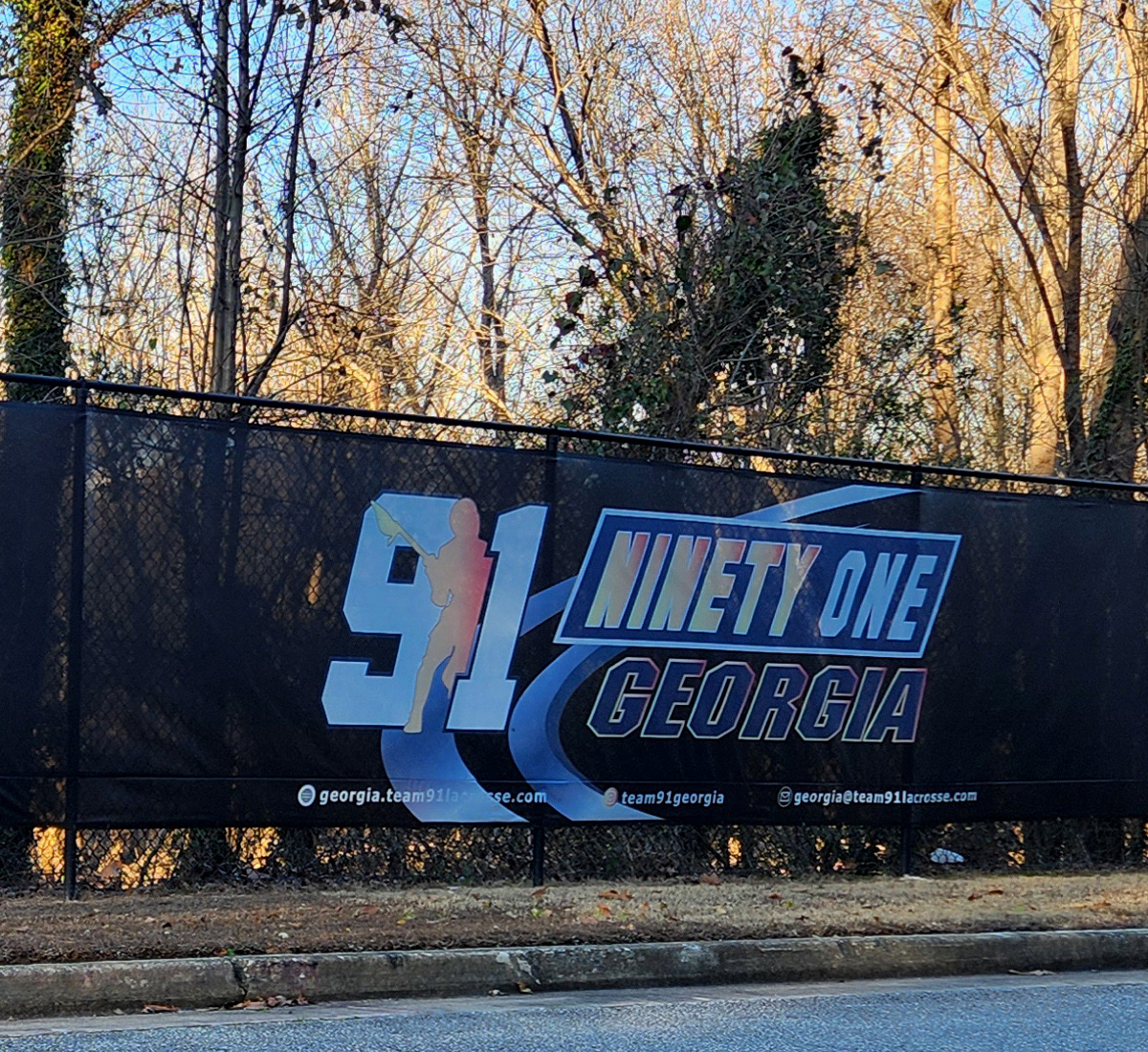 black fence windscreen on a fence along the side of a road, printed with a blue orange and white logo reading '91 ninety one Georgia'