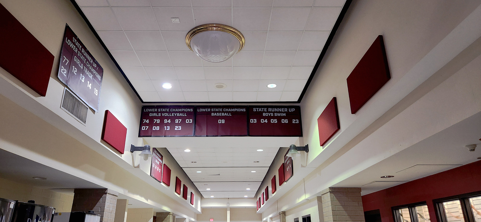 A maroon 10oz VCP windscren rectangular banner with white text and numbers promoting state champions for Wando High School. The banner is displayed on the upper part of the hall walls, lining the hall.