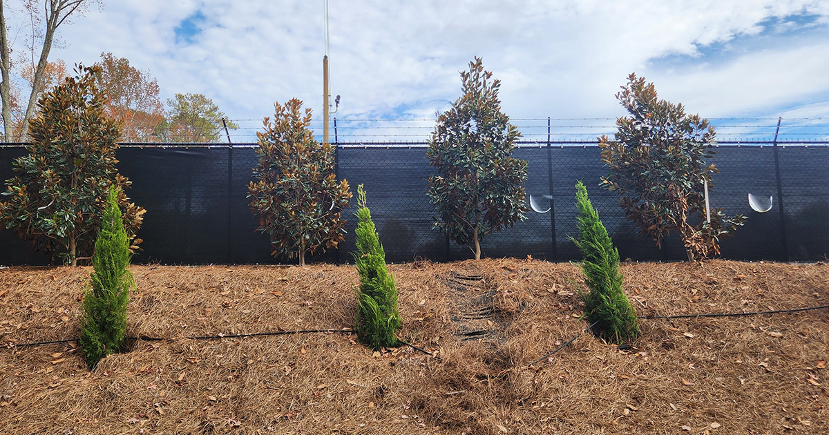 Close-up of a fence surrounding a business, covered with black privacy windscreen, highlighting installation around obstacles and uneven terrain.