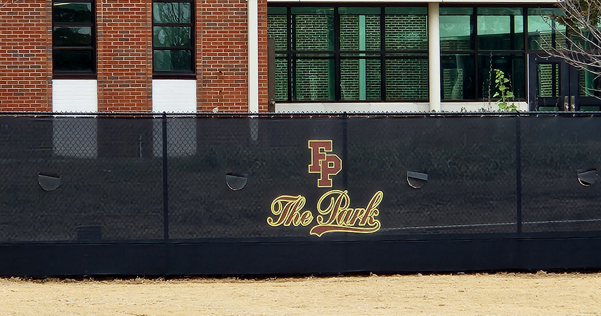 Black fence windscreen with half-moon vents, featuring the 'FP' logo above the text 'The Park' in cursive, both printed in maroon ink outlined in yellow.