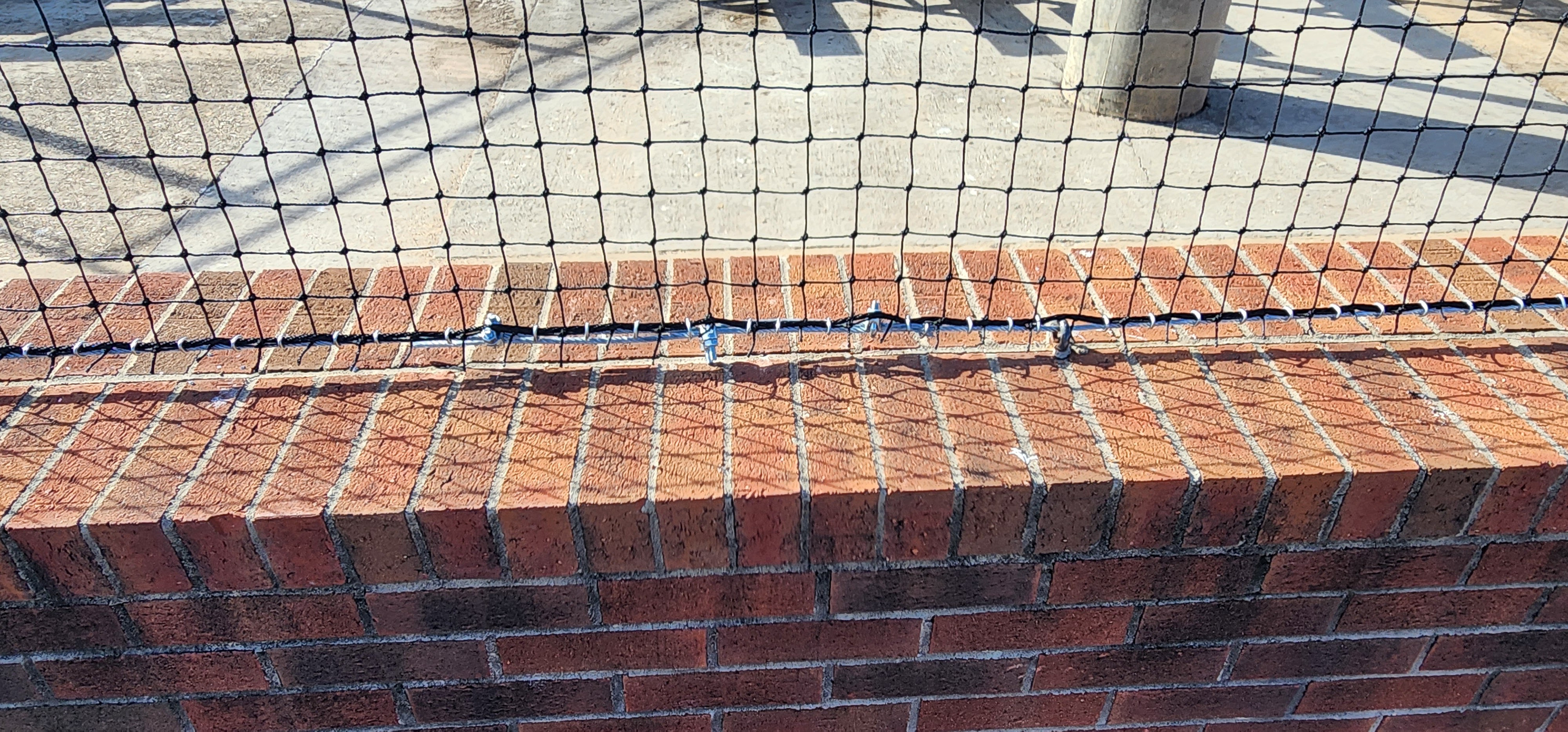 backstop black sports netting tension wire attachment to brick