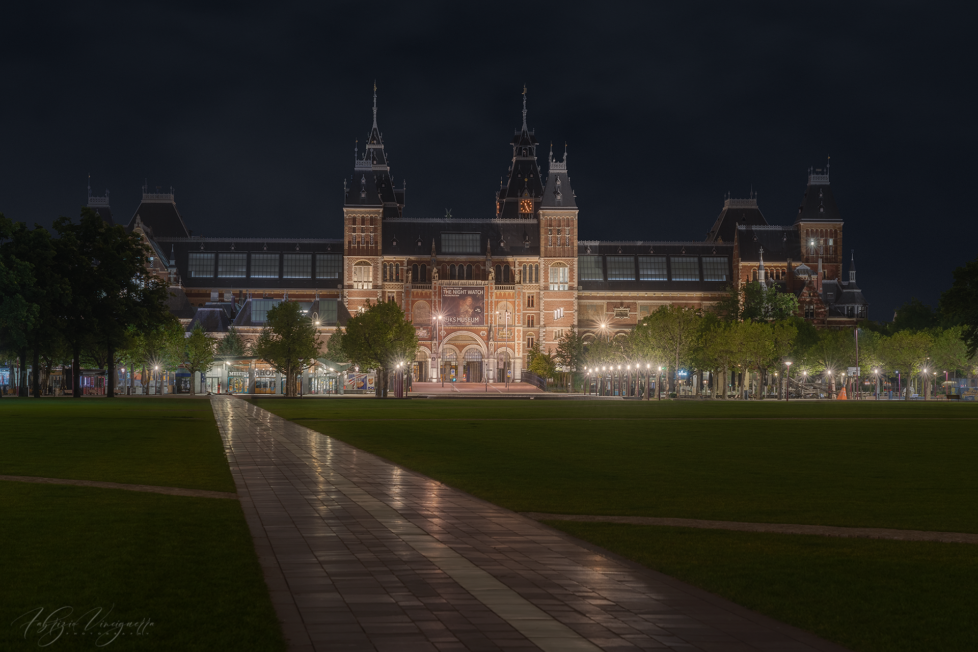 Rijksmuseum illuminato di notte – Il celebre museo di Amsterdam brilla sotto le luci artificiali, con il sentiero che guida lo sguardo verso la sua maestosità.