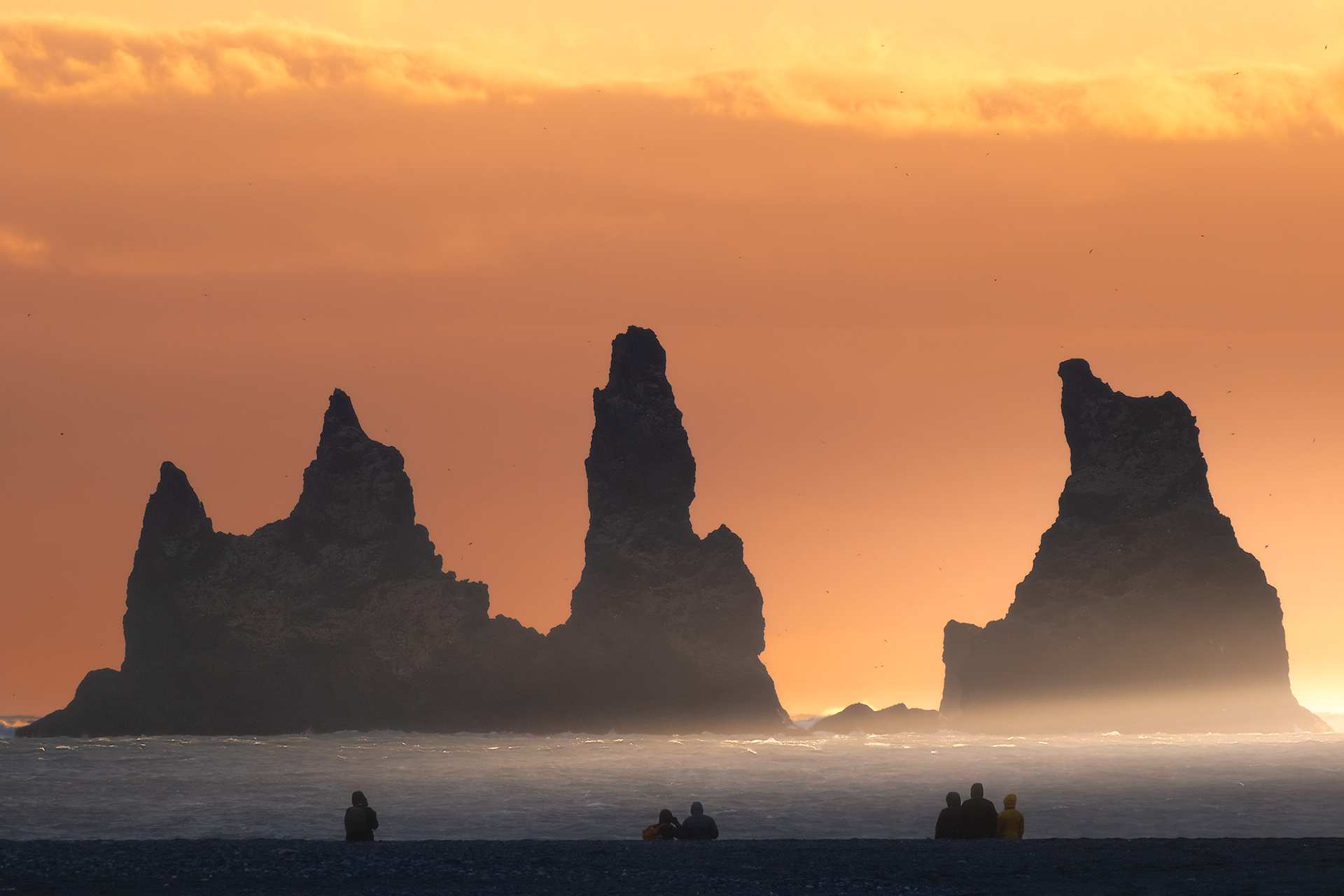 Faraglioni di Reynisdrangar con silhouette di persone – Un contrasto tra le imponenti formazioni rocciose e le piccole figure umane sulla spiaggia nera.