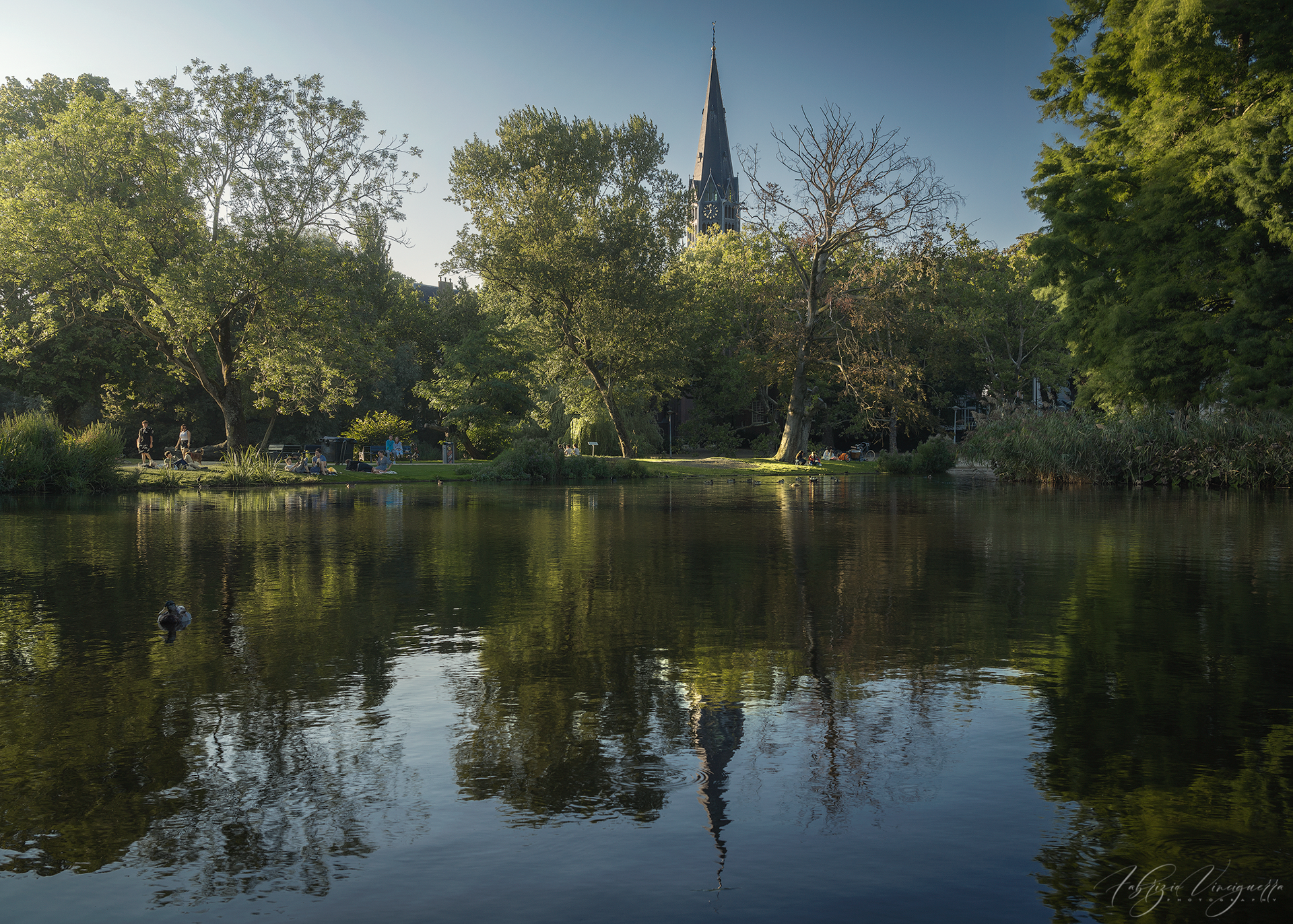  Parco con lago e chiesa sullo sfondo – Un angolo di natura nel cuore della città, dove il riflesso degli alberi e dell’architettura crea un’atmosfera rilassante.