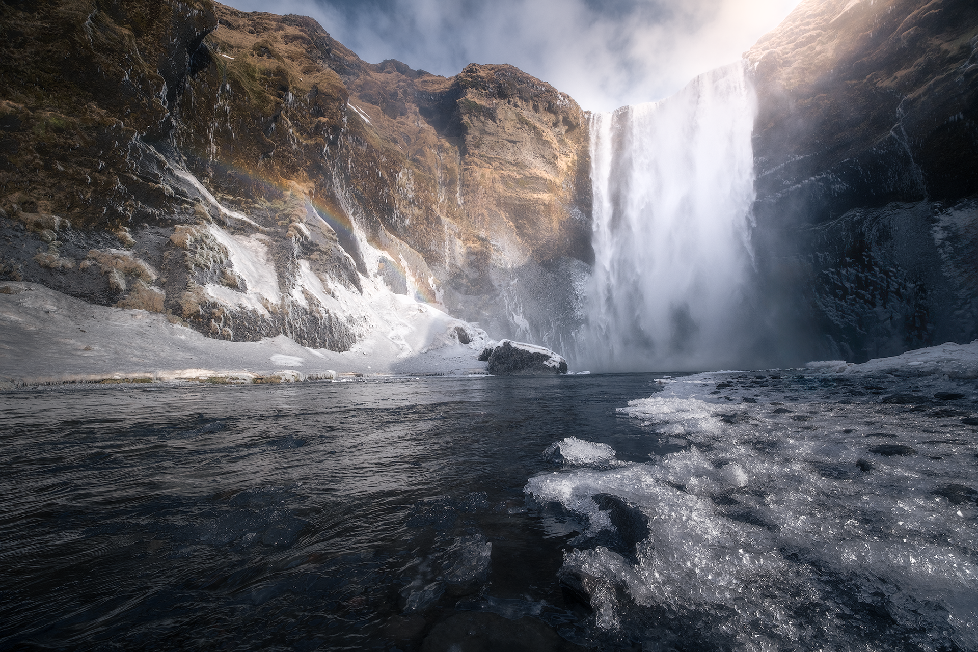 Cascata Skógafoss ghiacciata – Potente cascata islandese incorniciata da paesaggi invernali, con il fiume parzialmente ghiacciato e una luce soffusa che enfatizza l’atmosfera gelida.