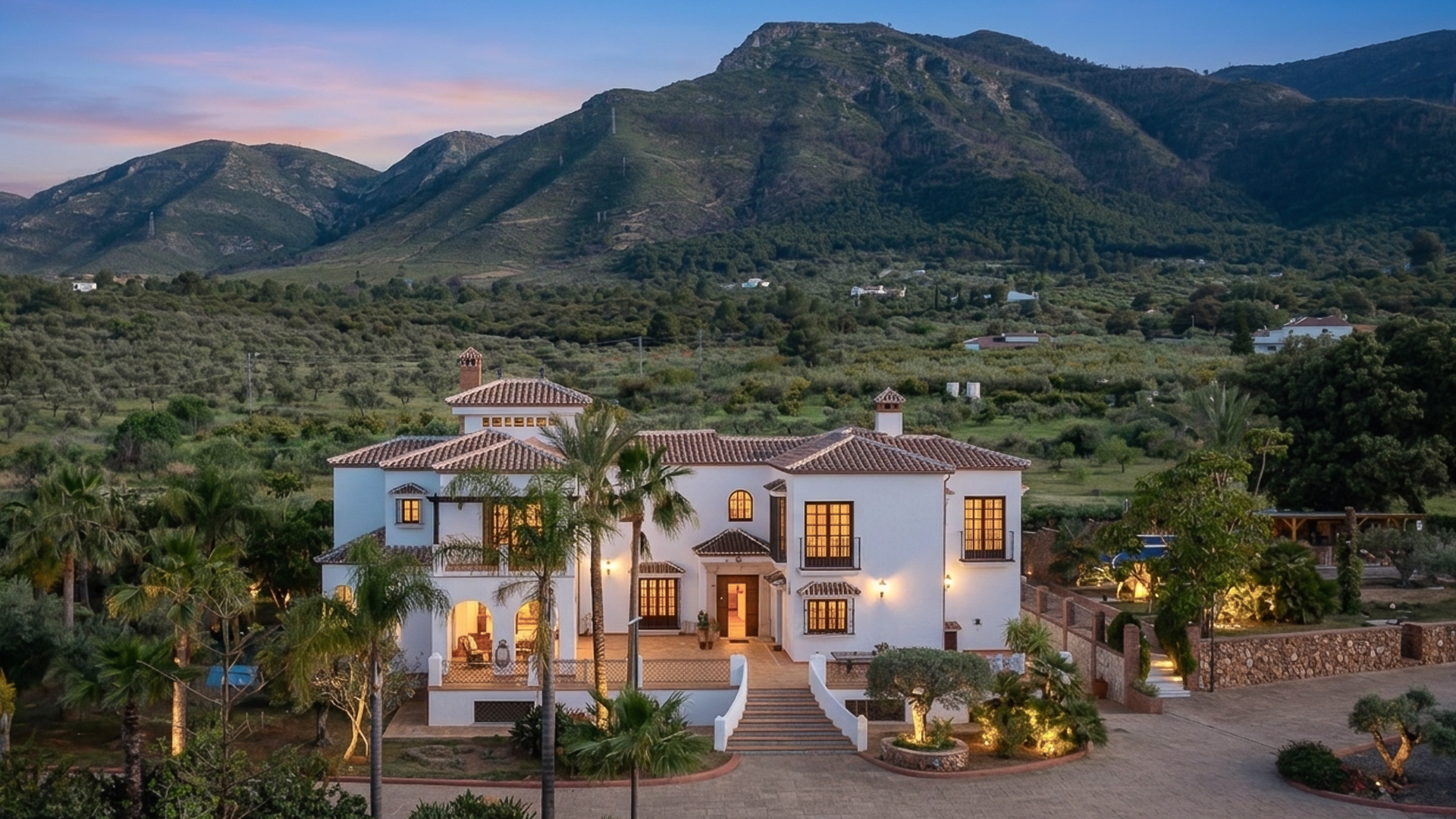 Luxury villa Loma Serena in Alhaurin el Grande at twilight with illuminated facade, palm trees and panoramic mountain views on the Costa del Sol.