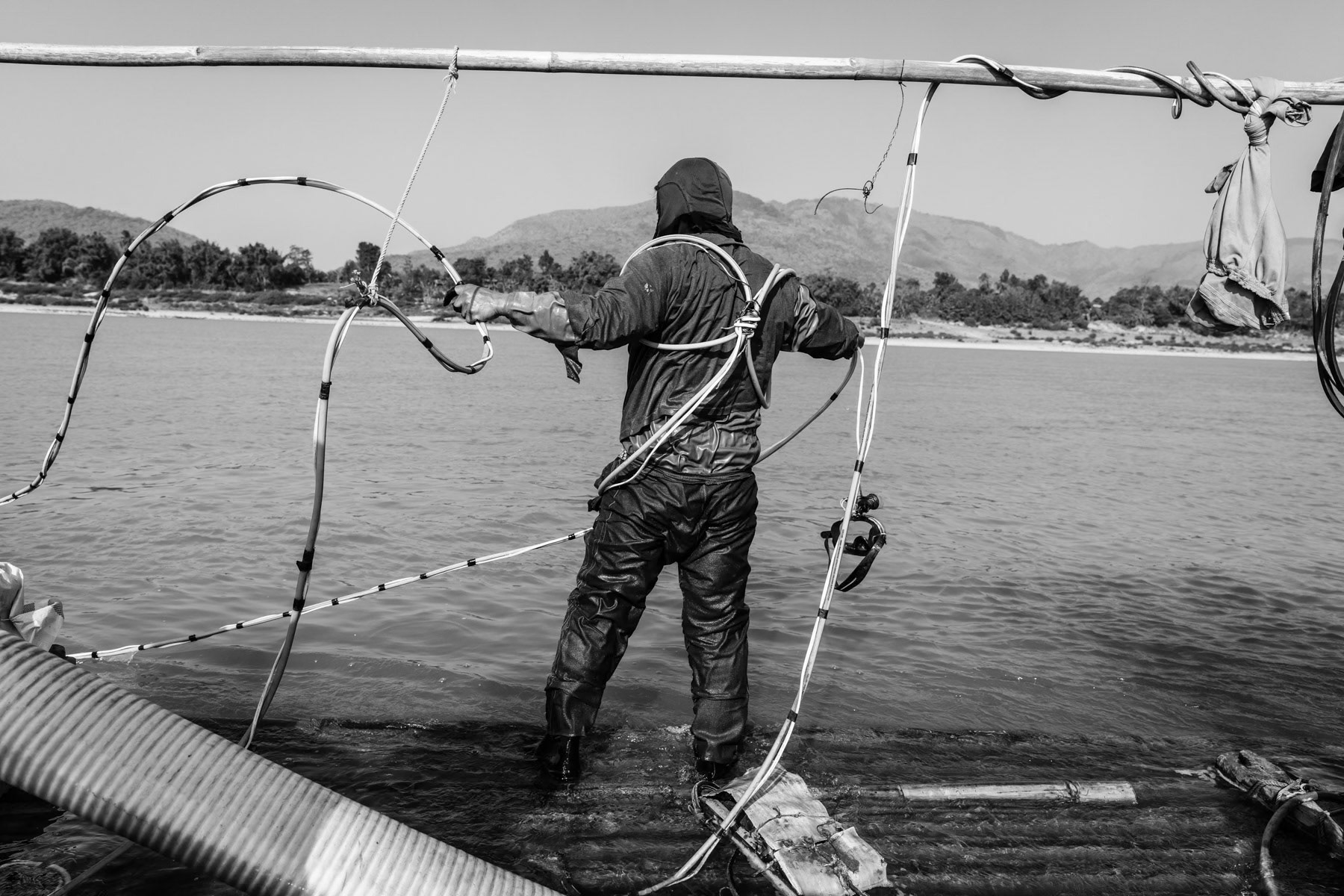 A gold diver getting ready to spend 3-4 hours underwater sucking up soil and sediment from the riverbed through a large hose. A team of 2 divers make in average 60 to 80 USD per day during the gold diving season between December and March. Irrawaddy River, Kachin State, Myanmar, February 2020