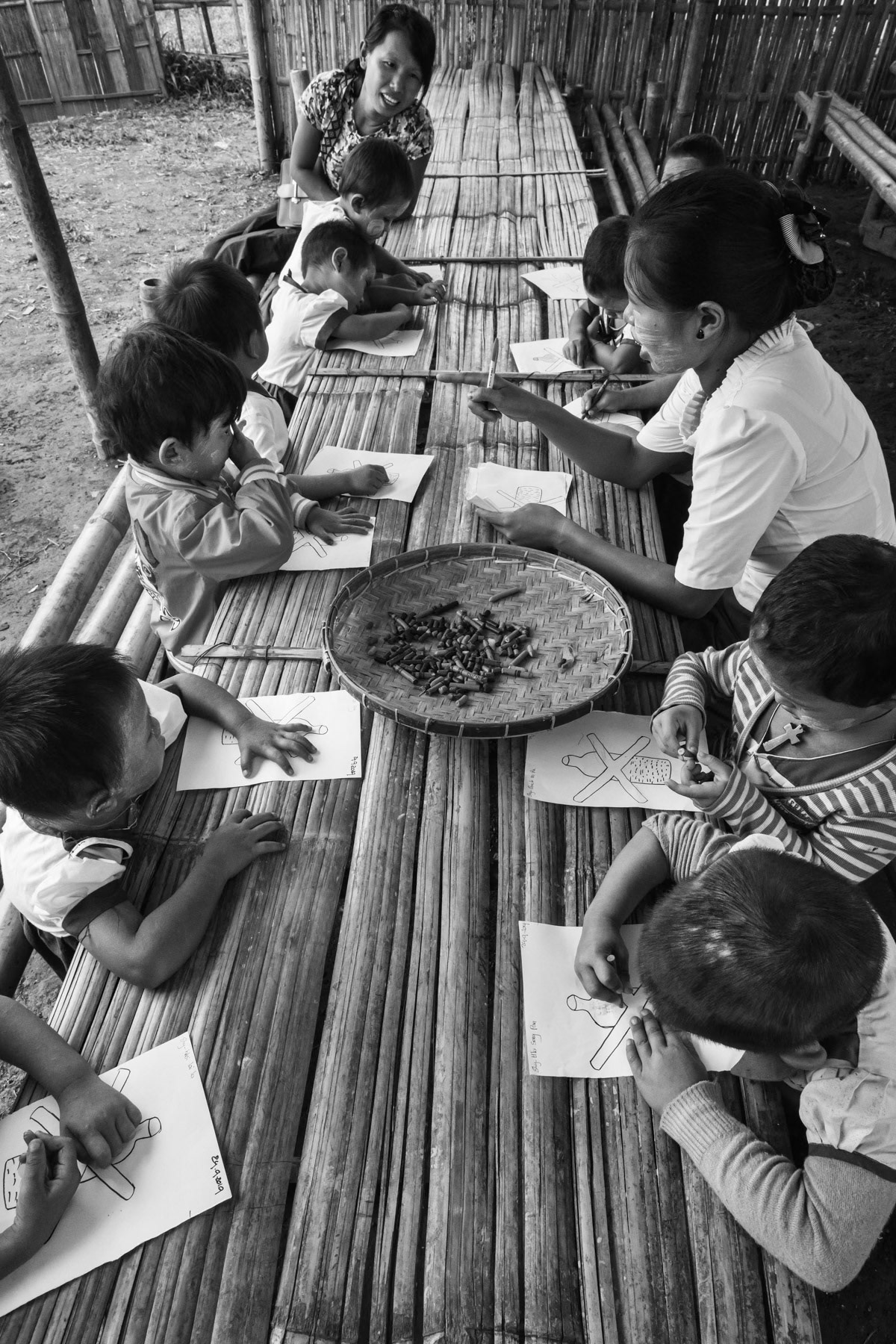 Small children at the kindergarden colouring the sign of plastic bottles harmful for the environment. St-Joseph IDP camp, Kachin State, Myanmar, September 2019
